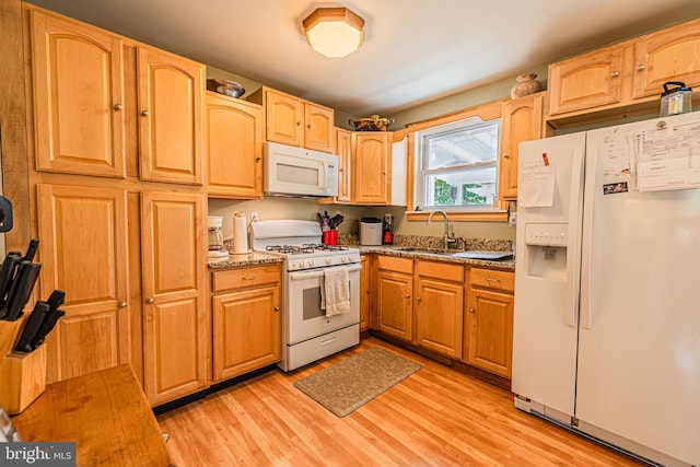 kitchen featuring stone countertops, white appliances, a sink, and light wood finished floors