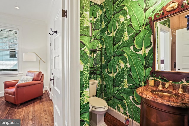 half bath with crown molding, baseboards, toilet, wood finished floors, and vanity