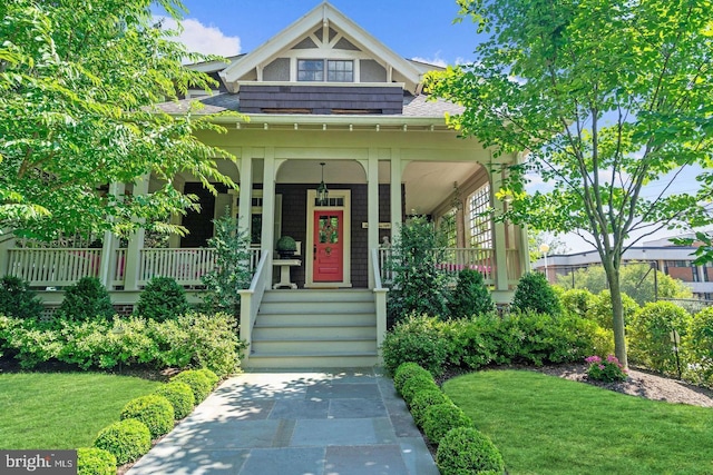 view of front facade with a front yard, covered porch, and roof with shingles