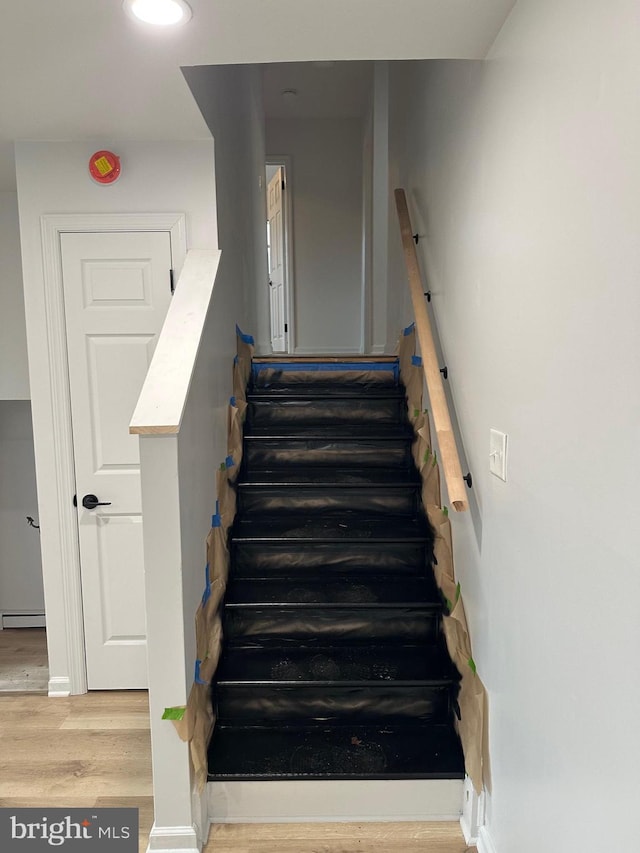 staircase with hardwood / wood-style floors and a baseboard heating unit