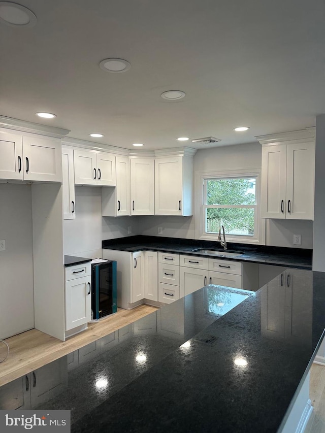 kitchen with sink, white cabinets, beverage cooler, and dark stone counters