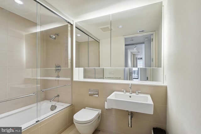 full bathroom with tile walls, sink, bath / shower combo with glass door, and toilet