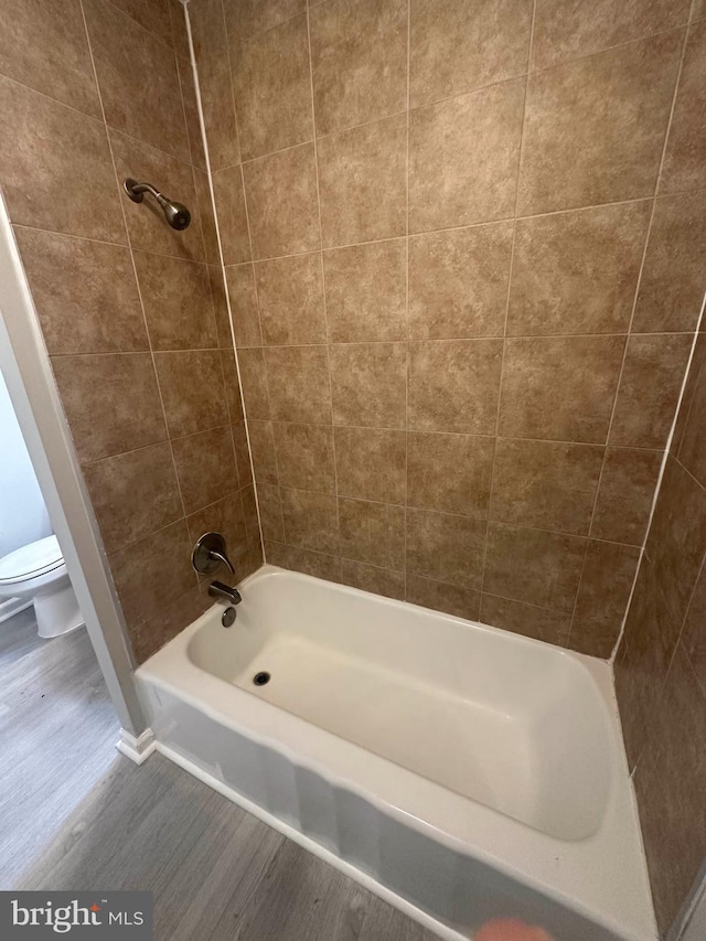 bathroom with tiled shower / bath, hardwood / wood-style flooring, and toilet