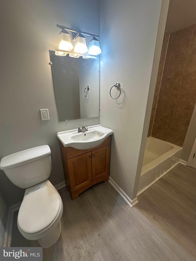 bathroom with a tile shower, vanity, hardwood / wood-style flooring, and toilet