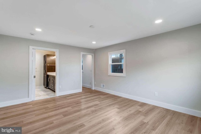 unfurnished bedroom with a walk in closet, ensuite bathroom, and light wood-type flooring