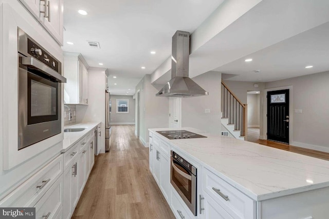 kitchen featuring sink, white cabinets, island exhaust hood, light stone counters, and stainless steel appliances