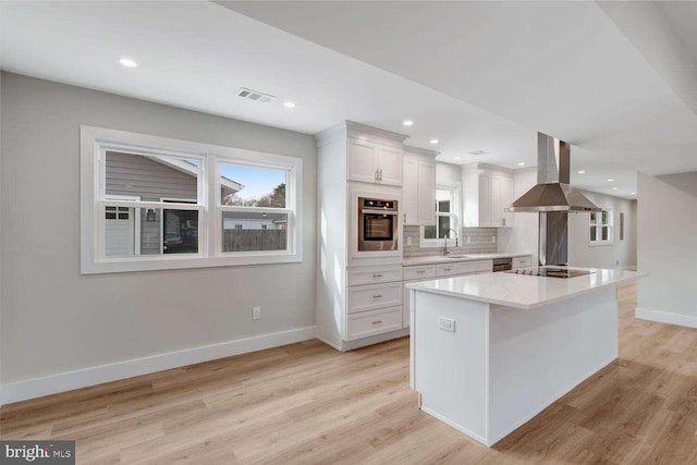 kitchen with island exhaust hood, white cabinets, a kitchen island, stainless steel oven, and light wood-type flooring