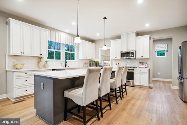 kitchen with a kitchen island, appliances with stainless steel finishes, decorative light fixtures, white cabinets, and backsplash