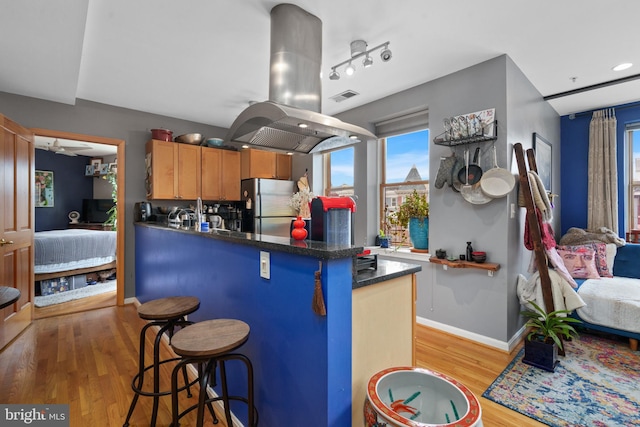 kitchen featuring stainless steel fridge, a breakfast bar, island range hood, kitchen peninsula, and light wood-type flooring