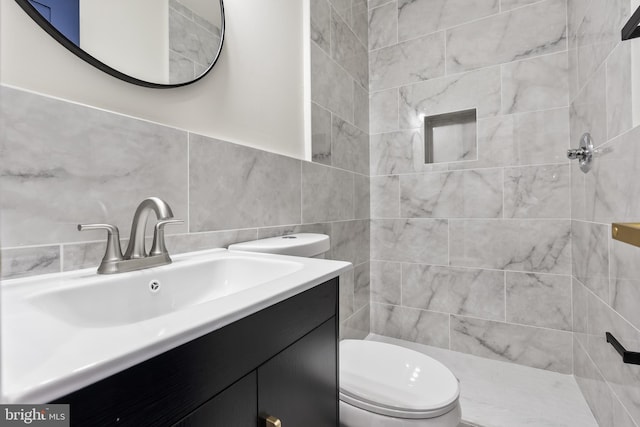 bathroom featuring tiled shower, vanity, toilet, and tile walls