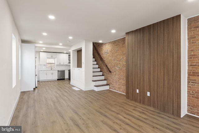 unfurnished living room featuring brick wall and light hardwood / wood-style flooring