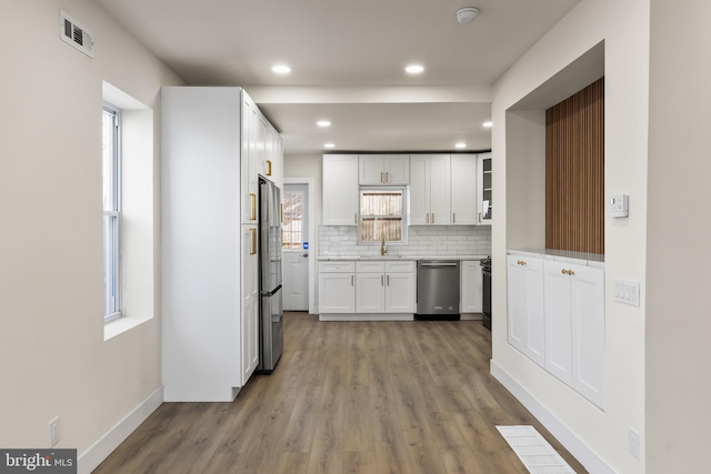 kitchen featuring sink, stainless steel appliances, wood-type flooring, white cabinets, and decorative backsplash