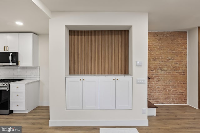 kitchen with light hardwood / wood-style flooring, appliances with stainless steel finishes, white cabinetry, backsplash, and brick wall