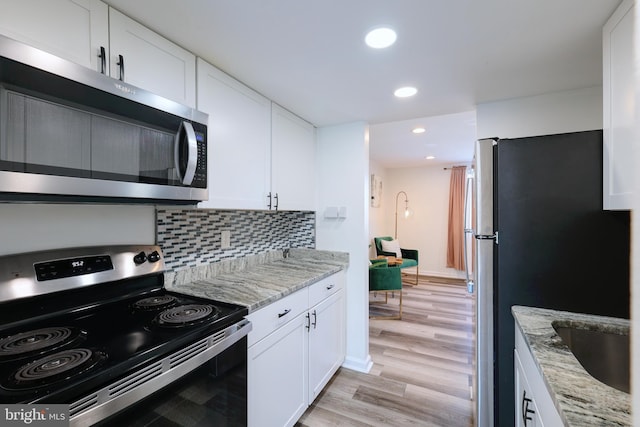 kitchen with white cabinets, stainless steel appliances, light stone countertops, light hardwood / wood-style floors, and backsplash