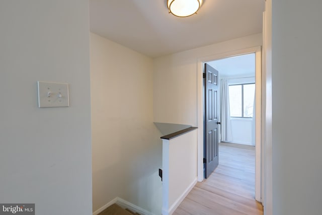 corridor featuring baseboards, an upstairs landing, and light wood finished floors