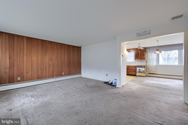 unfurnished living room with wooden walls, light carpet, and baseboard heating