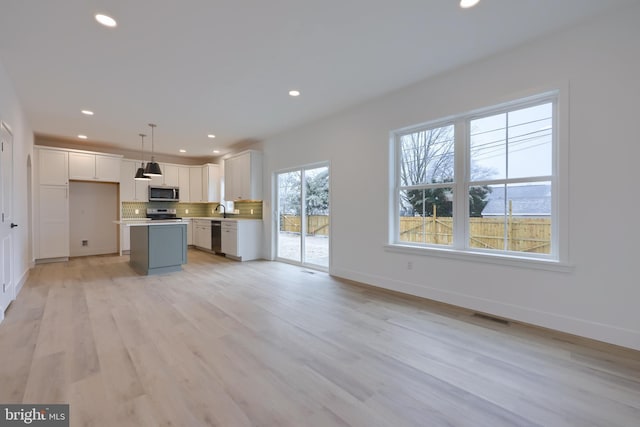 kitchen with appliances with stainless steel finishes, white cabinetry, hanging light fixtures, backsplash, and a center island