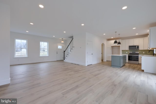 kitchen with appliances with stainless steel finishes, a kitchen island, pendant lighting, decorative backsplash, and white cabinets