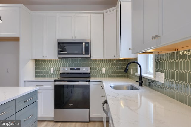 kitchen with appliances with stainless steel finishes, white cabinetry, sink, backsplash, and light stone counters