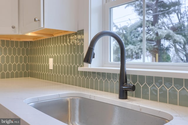 interior details featuring tasteful backsplash, sink, light stone counters, and white cabinets