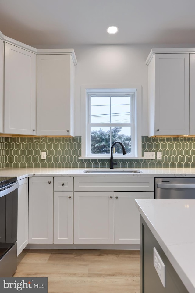 kitchen featuring white cabinetry, sink, decorative backsplash, stainless steel appliances, and light wood-type flooring