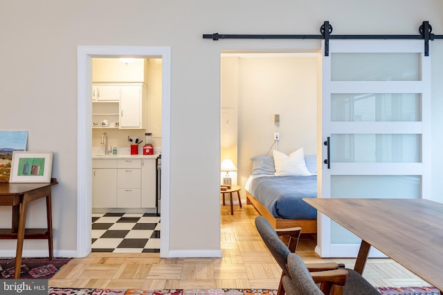 bedroom with light parquet flooring, a barn door, sink, and connected bathroom