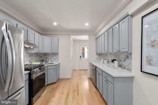 kitchen with sink, gray cabinetry, light wood-type flooring, ornamental molding, and stainless steel appliances