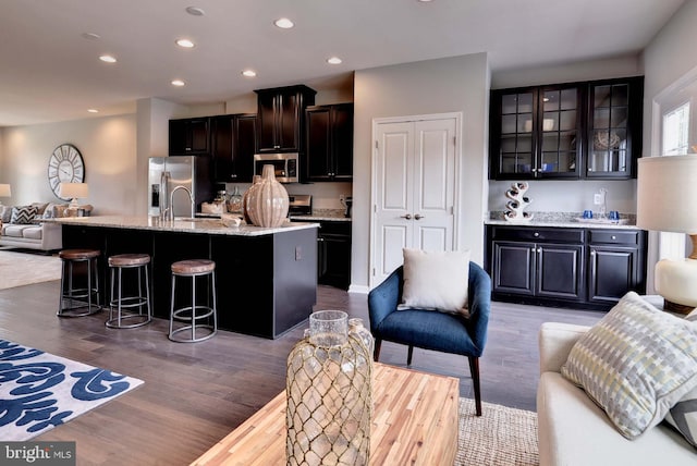 kitchen with appliances with stainless steel finishes, glass insert cabinets, open floor plan, an island with sink, and wood finished floors