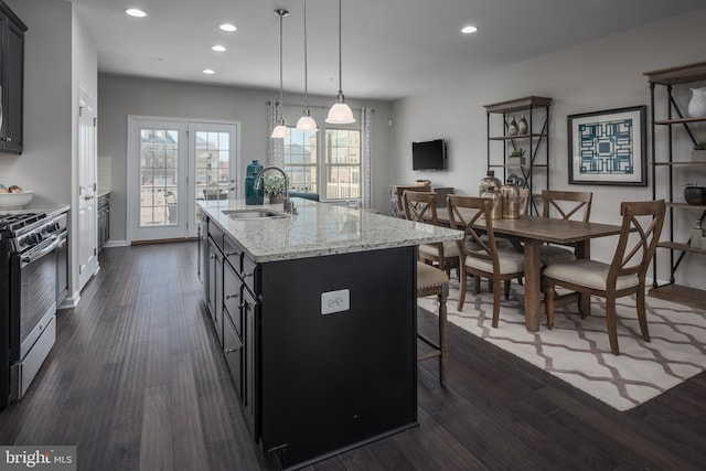 kitchen with stainless steel gas range oven, an island with sink, dark wood-style flooring, pendant lighting, and a sink