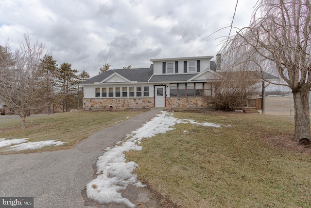 traditional-style house with stone siding, driveway, and a front lawn