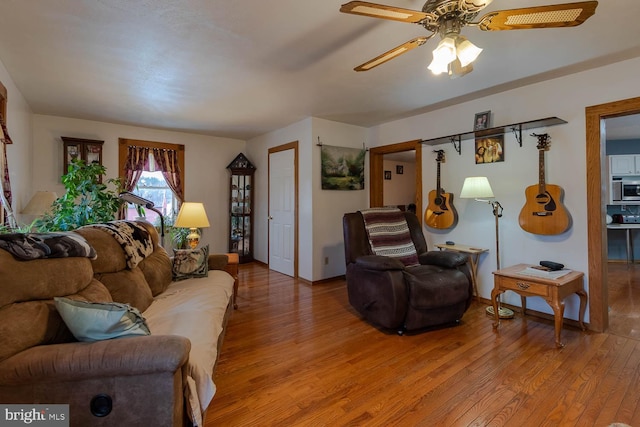 living area with light wood finished floors, a ceiling fan, and baseboards