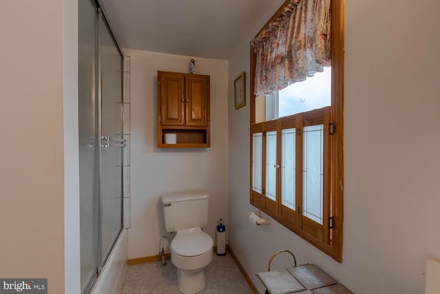 bathroom with toilet, baseboards, and combined bath / shower with glass door