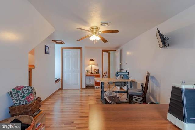 home office with a ceiling fan, heating unit, visible vents, and light wood-style floors