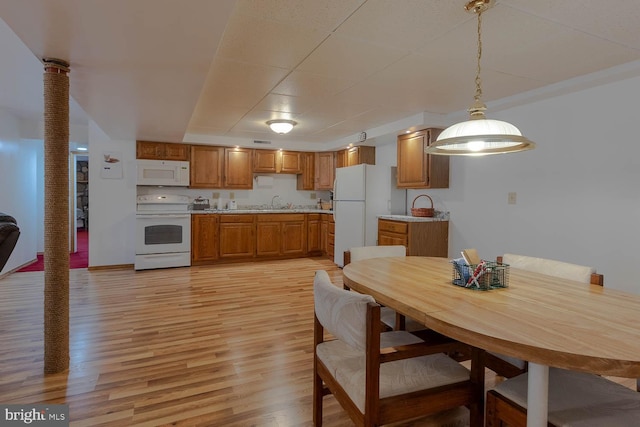 kitchen featuring pendant lighting, brown cabinets, light countertops, light wood-style flooring, and white appliances