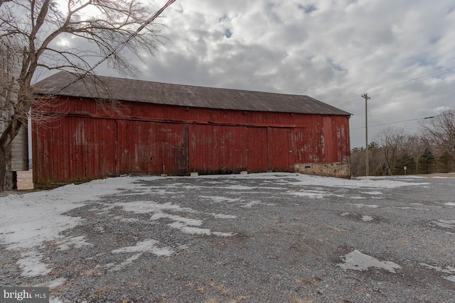 snow covered structure with an outbuilding, gravel driveway, and a barn