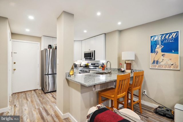 kitchen with white cabinetry, sink, kitchen peninsula, stainless steel appliances, and light stone countertops