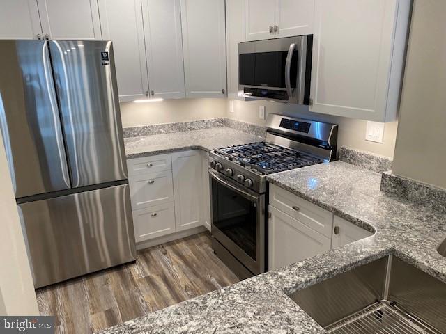 kitchen with sink, light stone counters, light hardwood / wood-style flooring, stainless steel appliances, and white cabinets