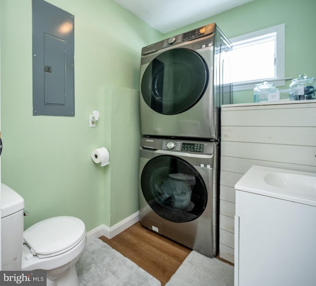 clothes washing area with electric panel, light hardwood / wood-style floors, and stacked washer / dryer