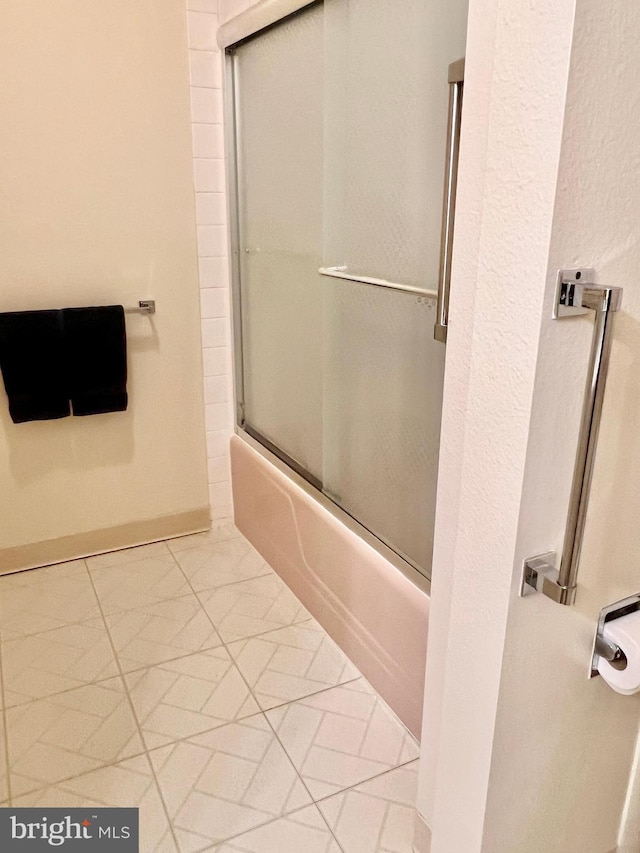 bathroom featuring combined bath / shower with glass door and baseboards