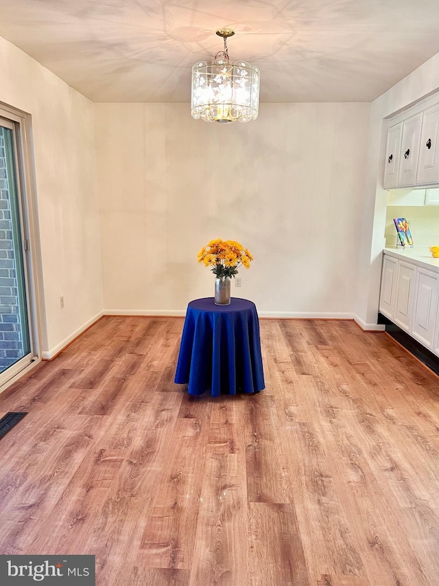 unfurnished dining area featuring a notable chandelier, baseboards, and light wood-style floors