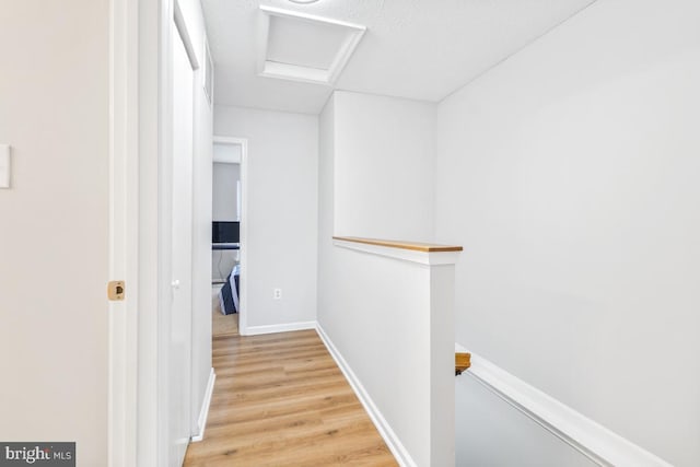 corridor with attic access, baseboards, light wood-style flooring, and an upstairs landing