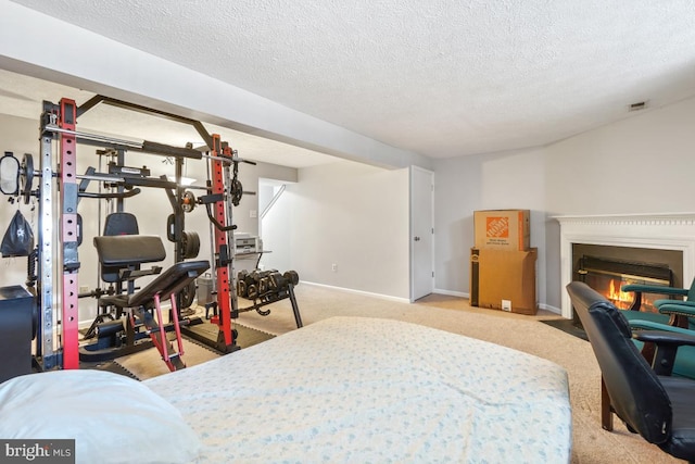 bedroom featuring light carpet, baseboards, visible vents, a glass covered fireplace, and a textured ceiling