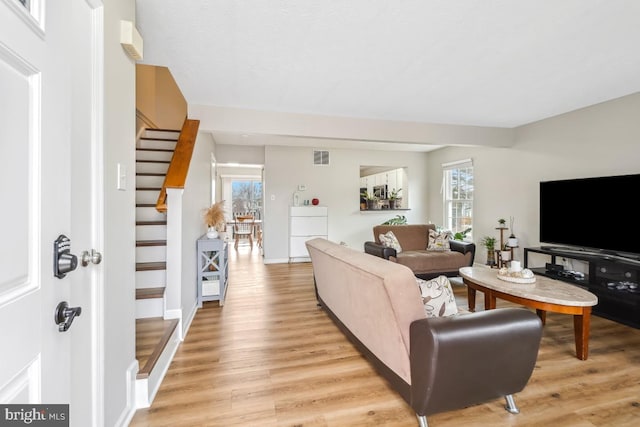 living area featuring stairs, light wood-type flooring, visible vents, and baseboards