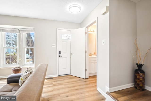 entryway with visible vents, a textured ceiling, light wood-style flooring, and baseboards