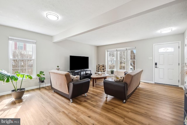 living area featuring light wood-style flooring, beam ceiling, baseboards, and a textured ceiling