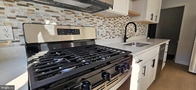 kitchen featuring gas range, white cabinetry, light stone countertops, and sink