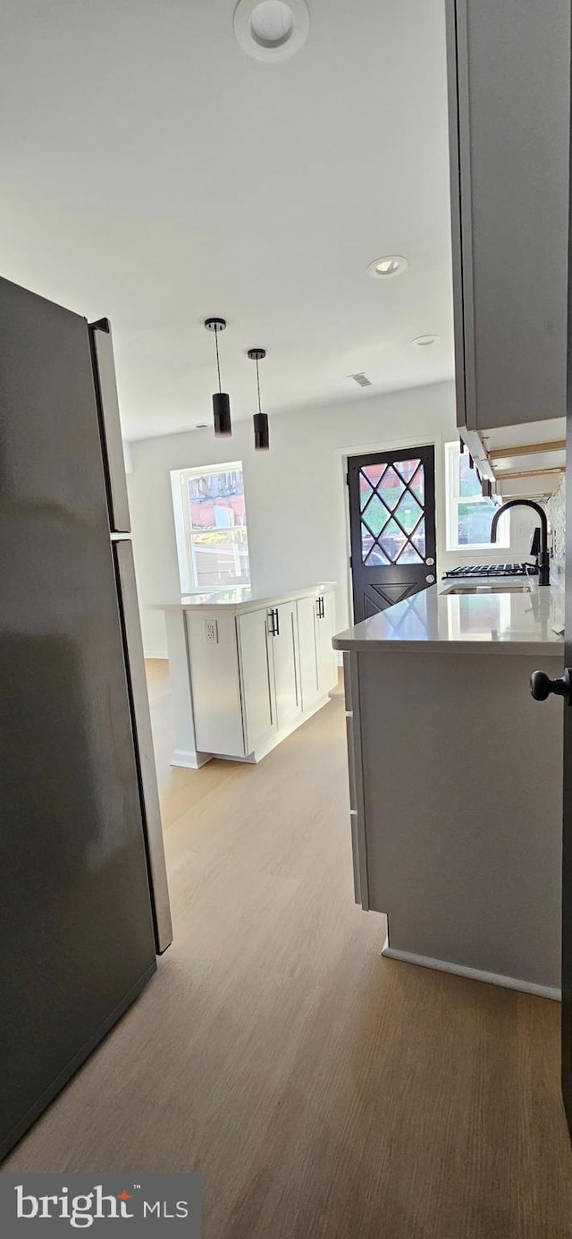 kitchen featuring sink, decorative light fixtures, stainless steel fridge, light hardwood / wood-style floors, and white cabinets