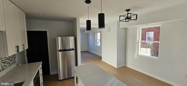 kitchen featuring white cabinetry, hanging light fixtures, stainless steel refrigerator, light stone countertops, and light hardwood / wood-style floors