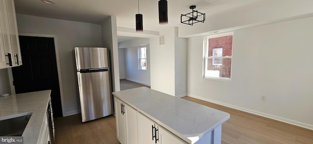 kitchen featuring stainless steel refrigerator, white cabinetry, light stone countertops, a kitchen island, and decorative light fixtures