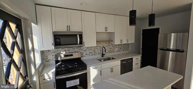 kitchen with appliances with stainless steel finishes, sink, white cabinets, and decorative light fixtures